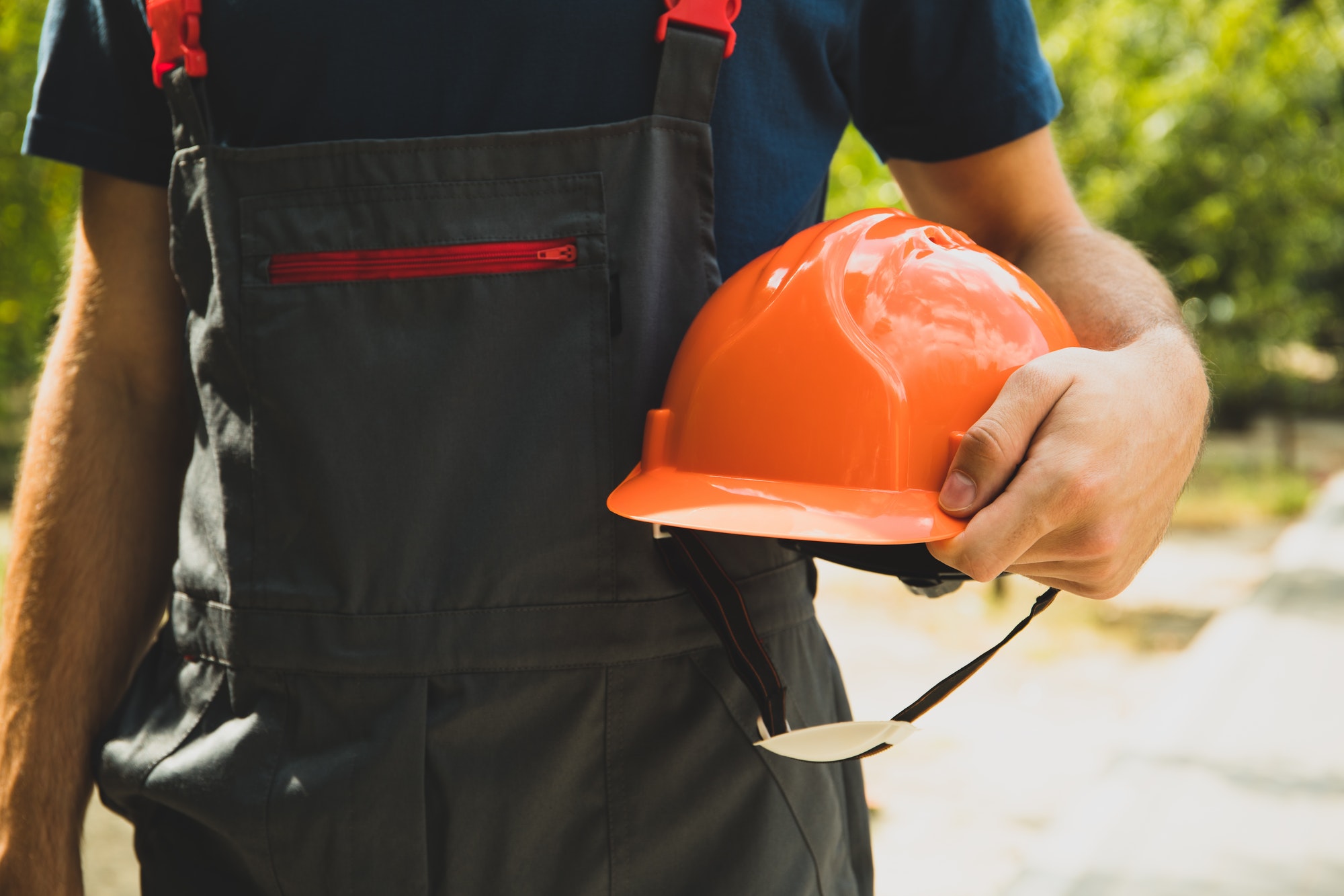 Man in overalls holds safety helmet outdoor